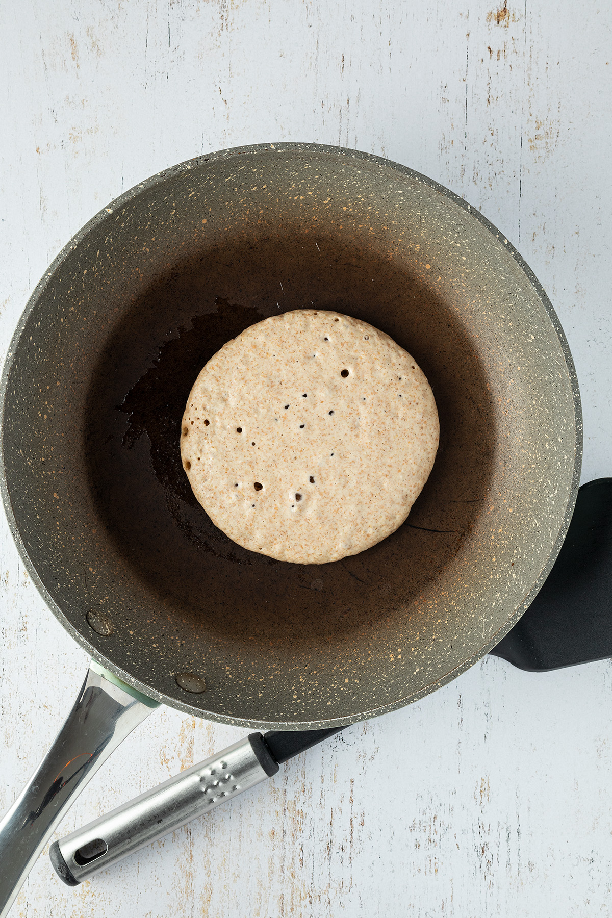 Pancake in einer Pfanne die kleinen Blasen auf der Oberfl&auml;che und der leicht braune Rand des Pancakes zeigen an, dass er breit zum wenden ist