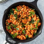 Vegetarische One Pot Pasta wird in einer Gusseisenpfanne serviert. Ein Tellerstapel im oberen Bildrand.