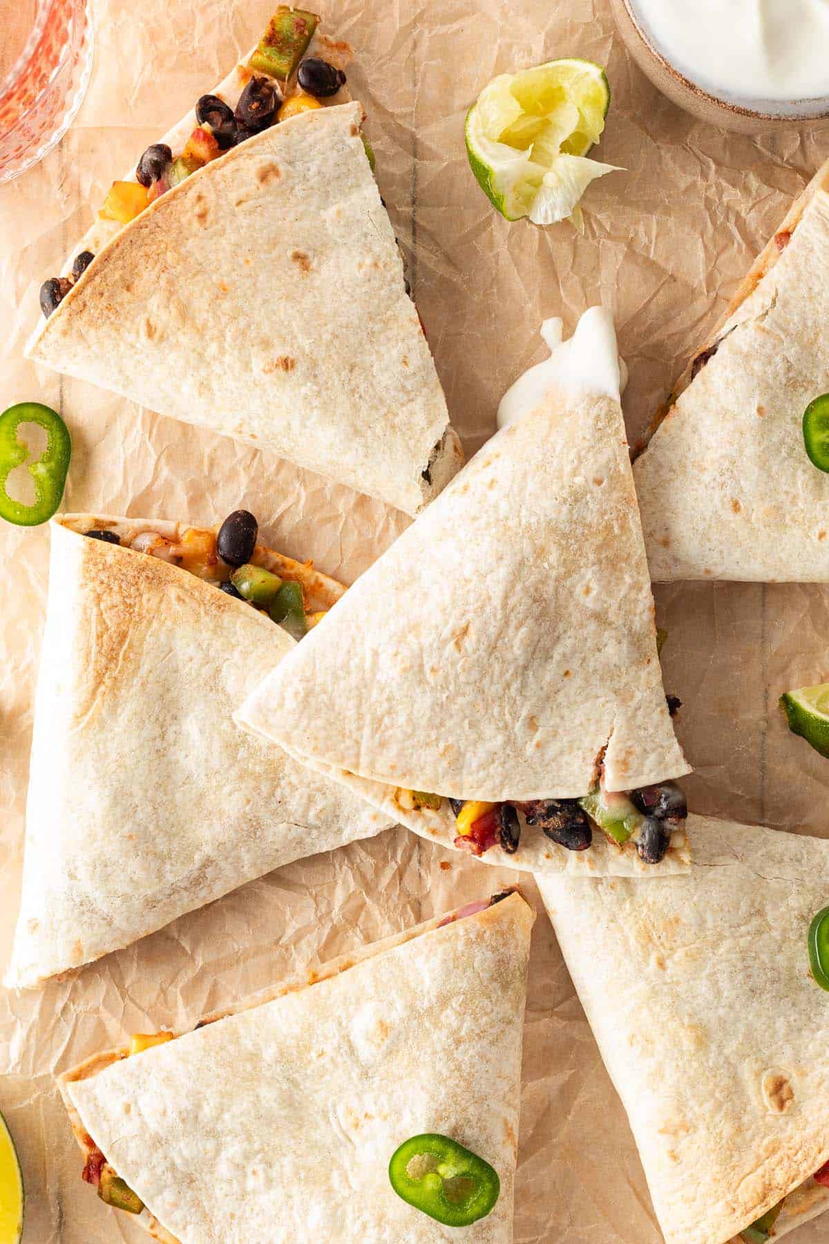 In Dreiecke geschnittene Quesadillas mit K&auml;se-Bohnen-Gem&uuml;se-F&uuml;llung auf einem Backpapier mit Jalape&ntilde;os und Limetten.