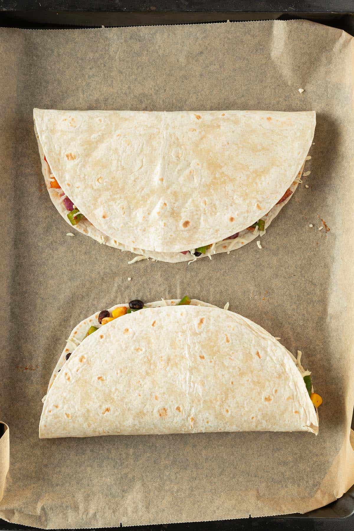 Zwei gef&uuml;llte und zusammengeklappte Tortillas auf ein mit Backpapier ausgelegtem Belch.