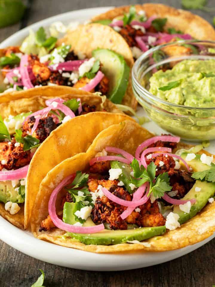 Ein Teller mit vegetarischen Tacos, die mit Tofu, Avocado und Zwiebeln gef&uuml;llt sind.