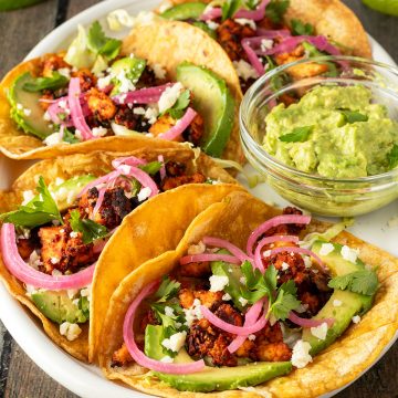 Vier vegetarische Tacos mit Tofu, Avocado und Zwiebeln auf einem Teller.