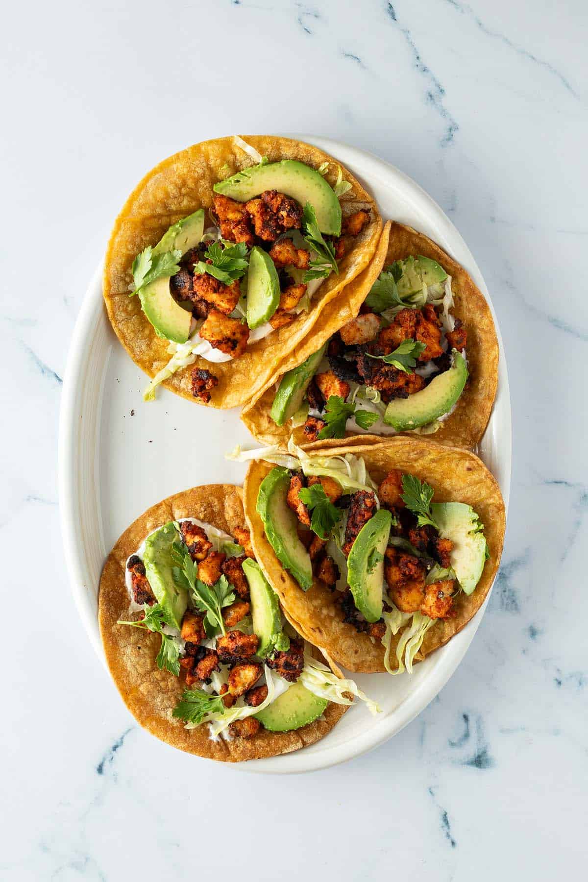 Teller mit vier Tacos, die mit Schmand, Tofu, Avocado und Salat belegt sind.