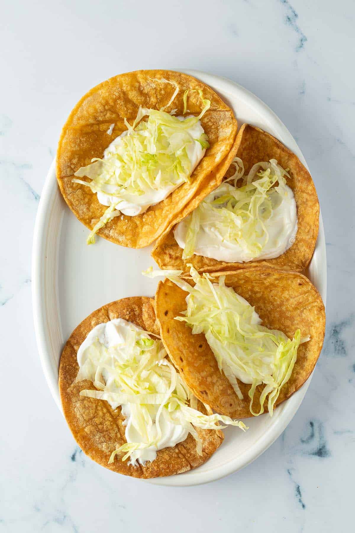Teller mit vier kleinen Tortillas, die mit Schmand und Salat getoppt sind.
