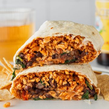 Zwei Burrito H&auml;lften liegen aufeinander auf einem Teller, ein Glas und eine Flasche im Hintergrund.