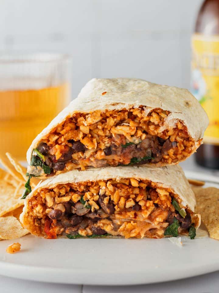 Zwei Burrito H&auml;lften liegen aufeinander auf einem Teller, ein Glas und eine Flasche im Hintergrund.