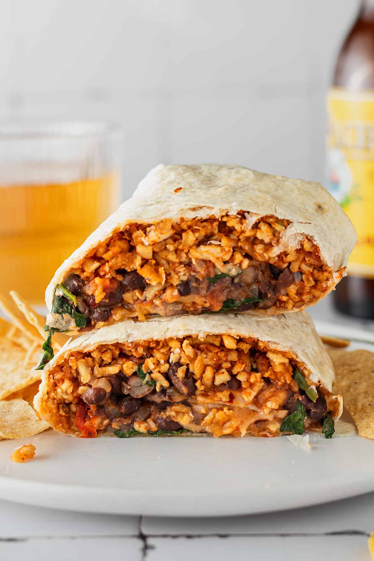 Zwei Burrito H&auml;lften liegen aufeinander auf einem Teller, ein Glas und eine Flasche im Hintergrund.