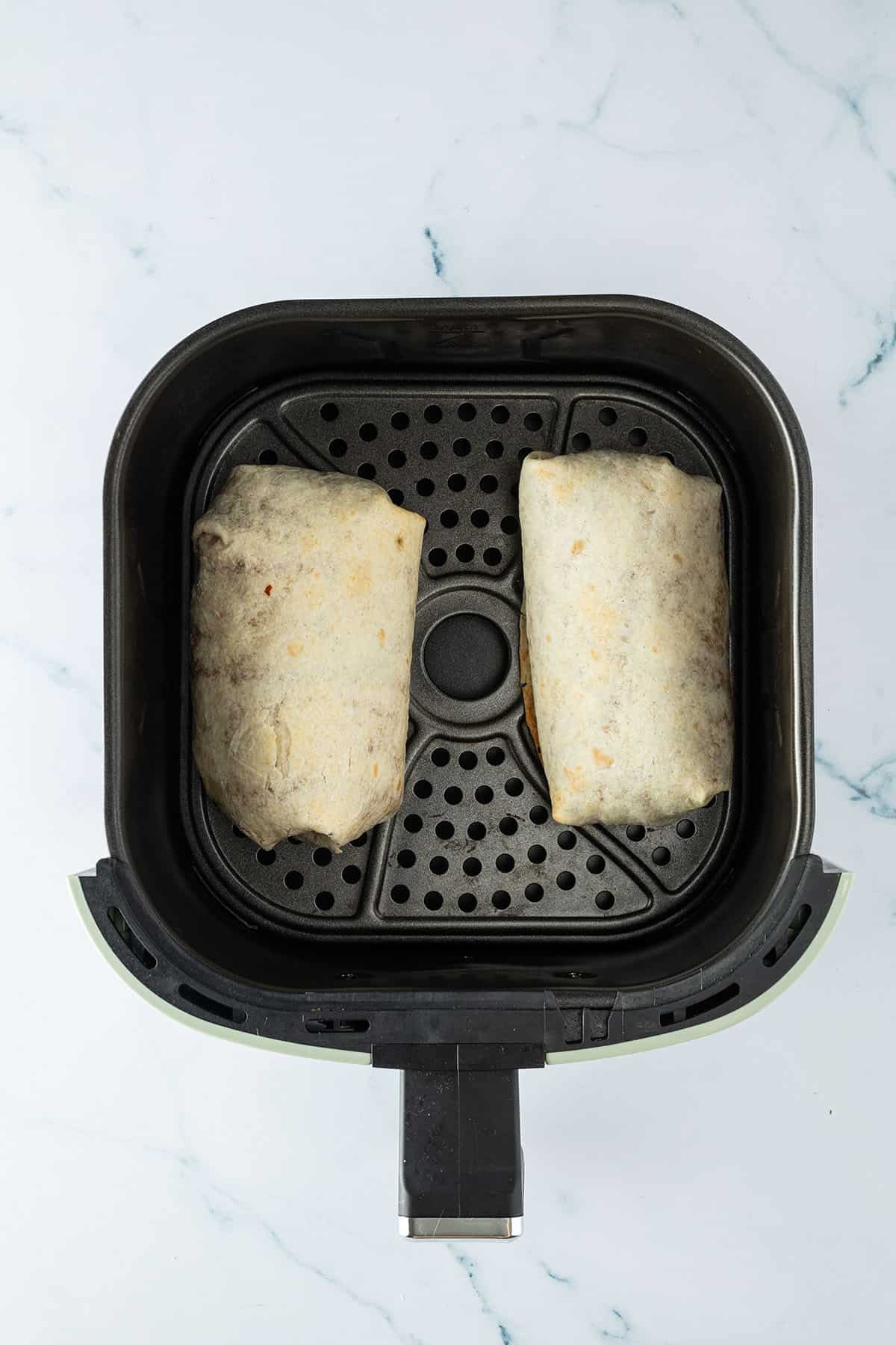 Zwei Burritos liegen nebeneinander in dem Korb einer Hei&szlig;luftfritteuse.
