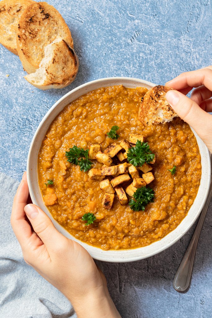 Vegetarischer Linseneintopf serviert mit knusprigen Tofu W&uuml;rfeln und getoasteten Brotscheiben, die in die Suppe eingetunkt werden.