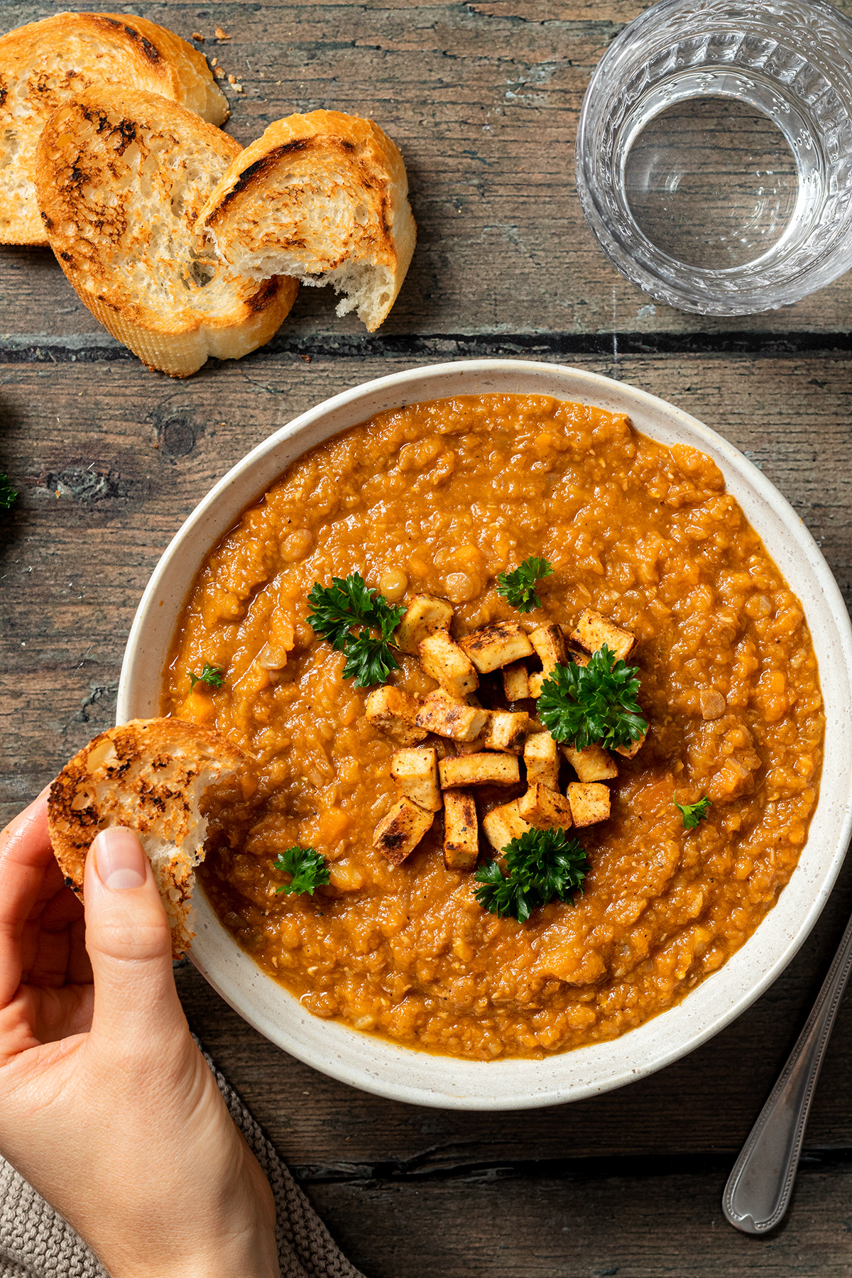 Vegetarischer Linseneintopf serviert mit knusprigen Tofu W&uuml;rfeln und getoasteten Brotscheiben, die in die Suppe eingetunkt werden.