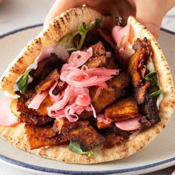Hand h&auml;lt ein vegetarischen Tofu D&ouml;ner mit eingelegten Zwiebeln, Gurke und Sprossen.
