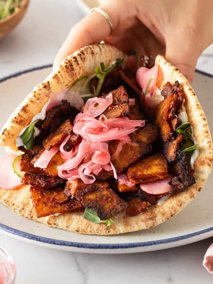 Hand h&auml;lt ein vegetarischen Tofu D&ouml;ner mit eingelegten Zwiebeln, Gurke und Sprossen.