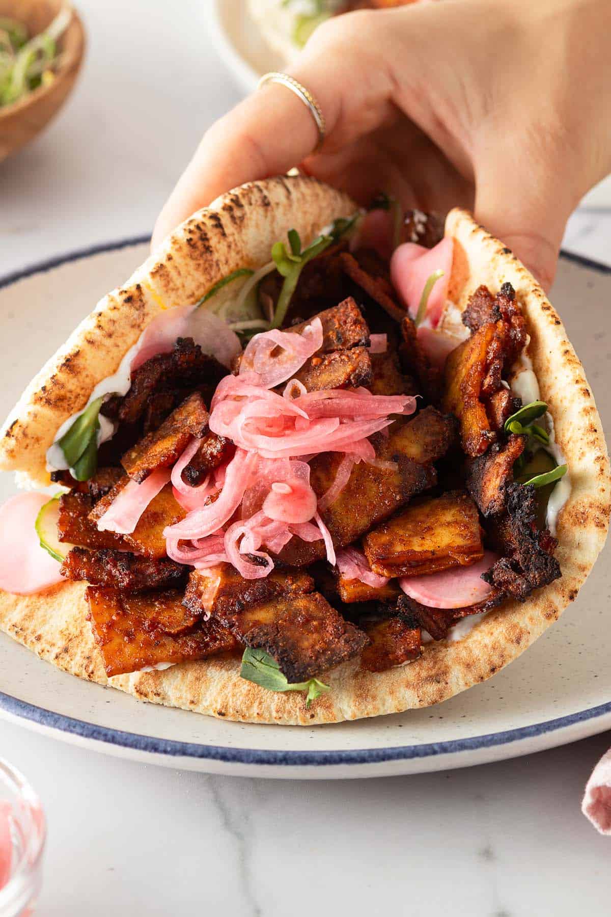 Hand h&auml;lt ein vegetarischen Tofu D&ouml;ner mit eingelegten Zwiebeln, Gurke und Sprossen.
