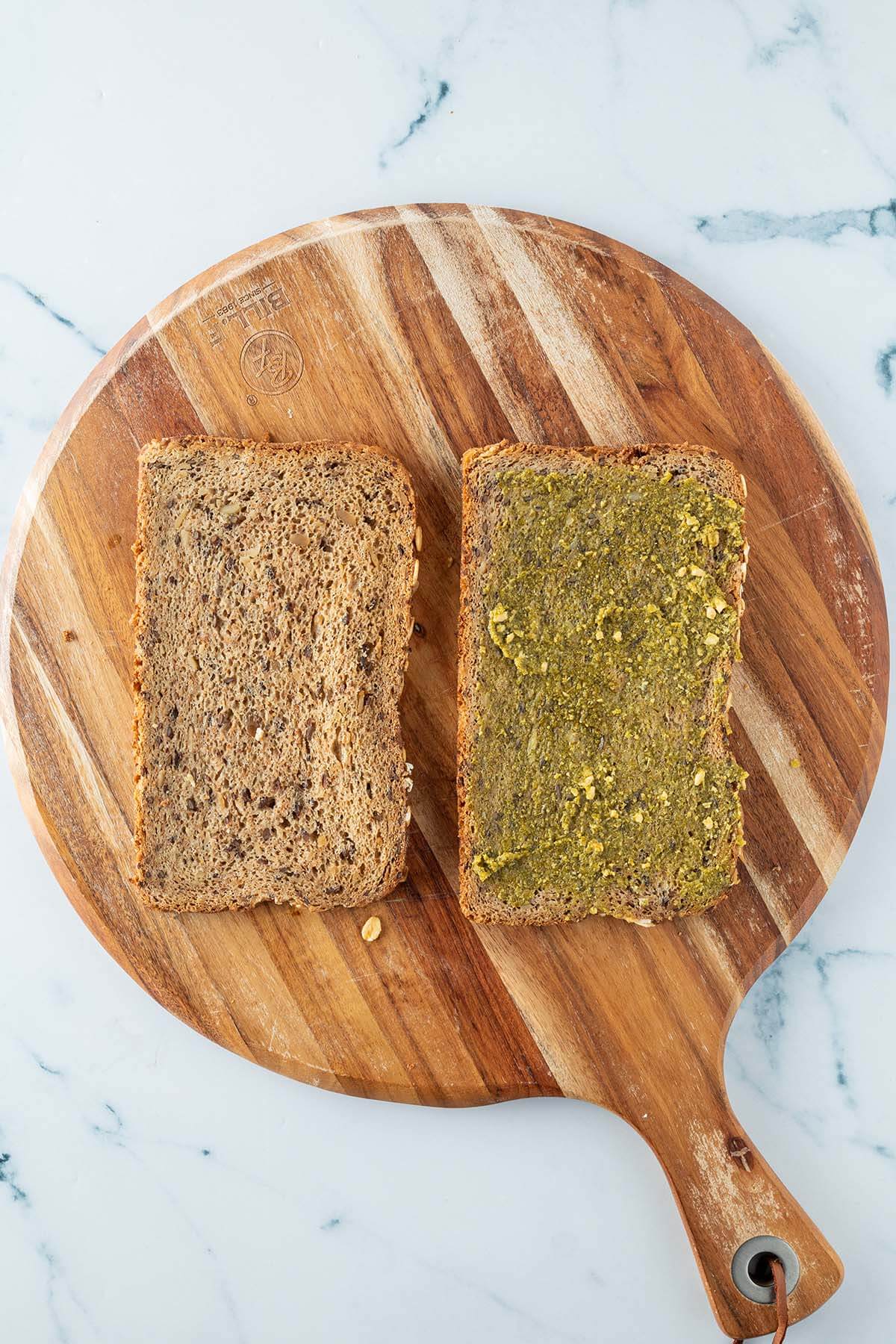 Zwei Brotscheiben auf einem Holzbrett, eine davon mit einem gr&uuml;nen Pesto-Aufstrich.