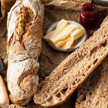 Zwei Vollkorn Baguette auf einem Tablett mit Butter und Marmelade.