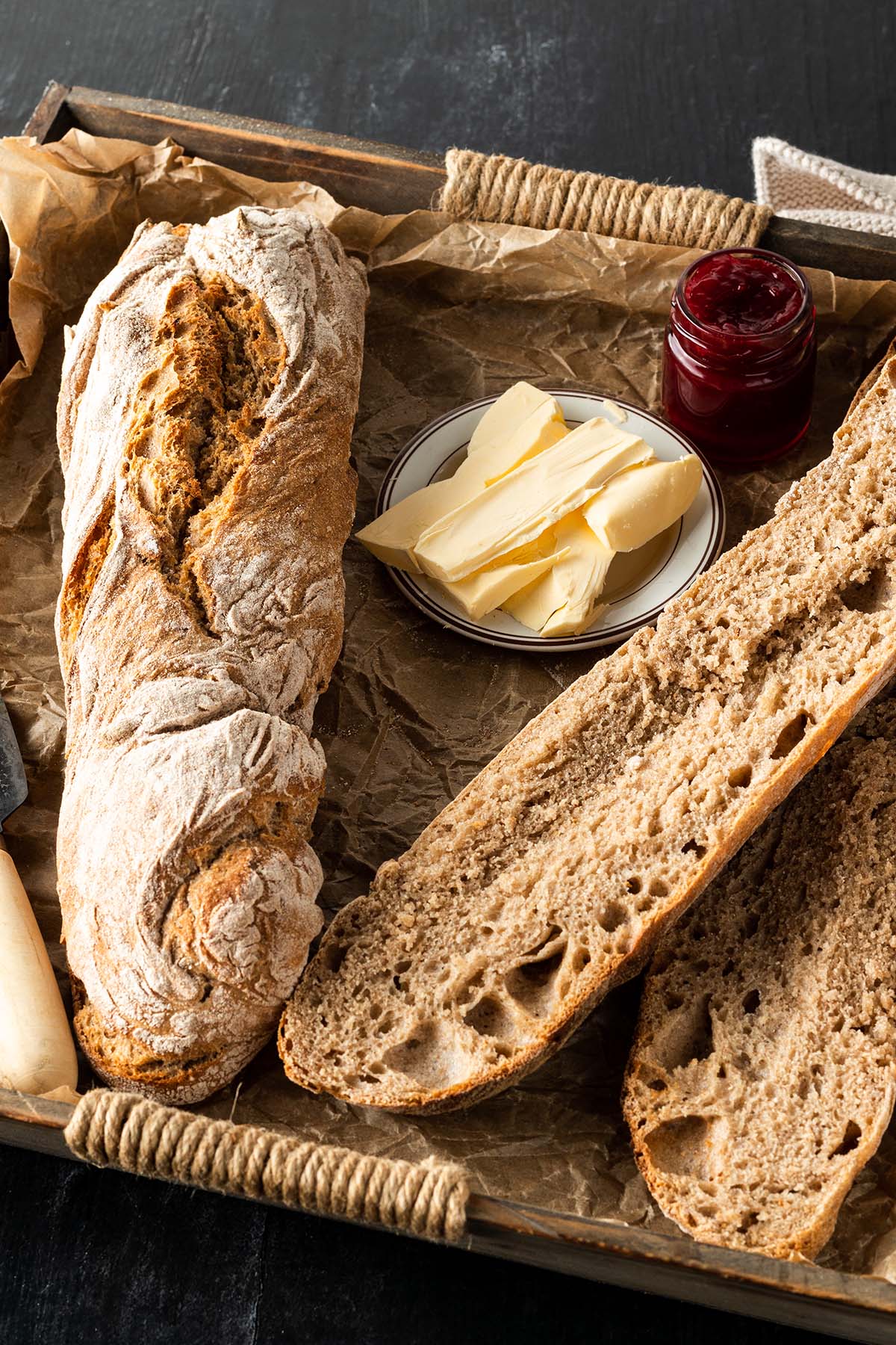 Zwei Vollkorn Baguette auf einem Tablett mit Butter und Marmelade.