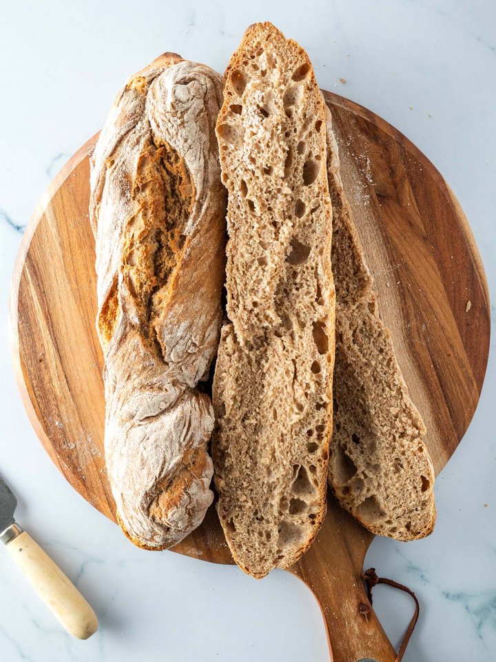 Zwei rustikale Vollkorn Baguette auf einem Holzbrett, eines davon aufgeschnitten.