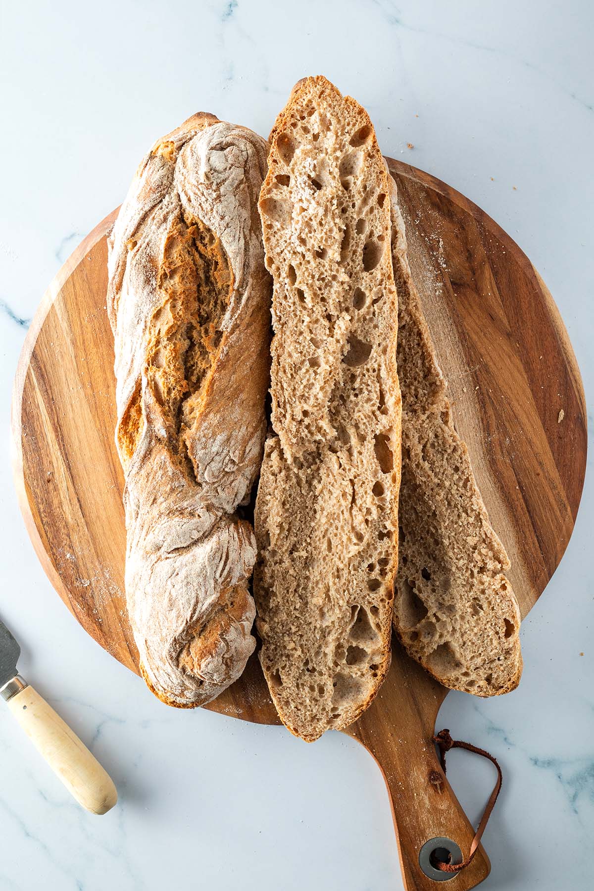 Zwei rustikale Vollkorn Baguette auf einem Holzbrett, eines davon aufgeschnitten.