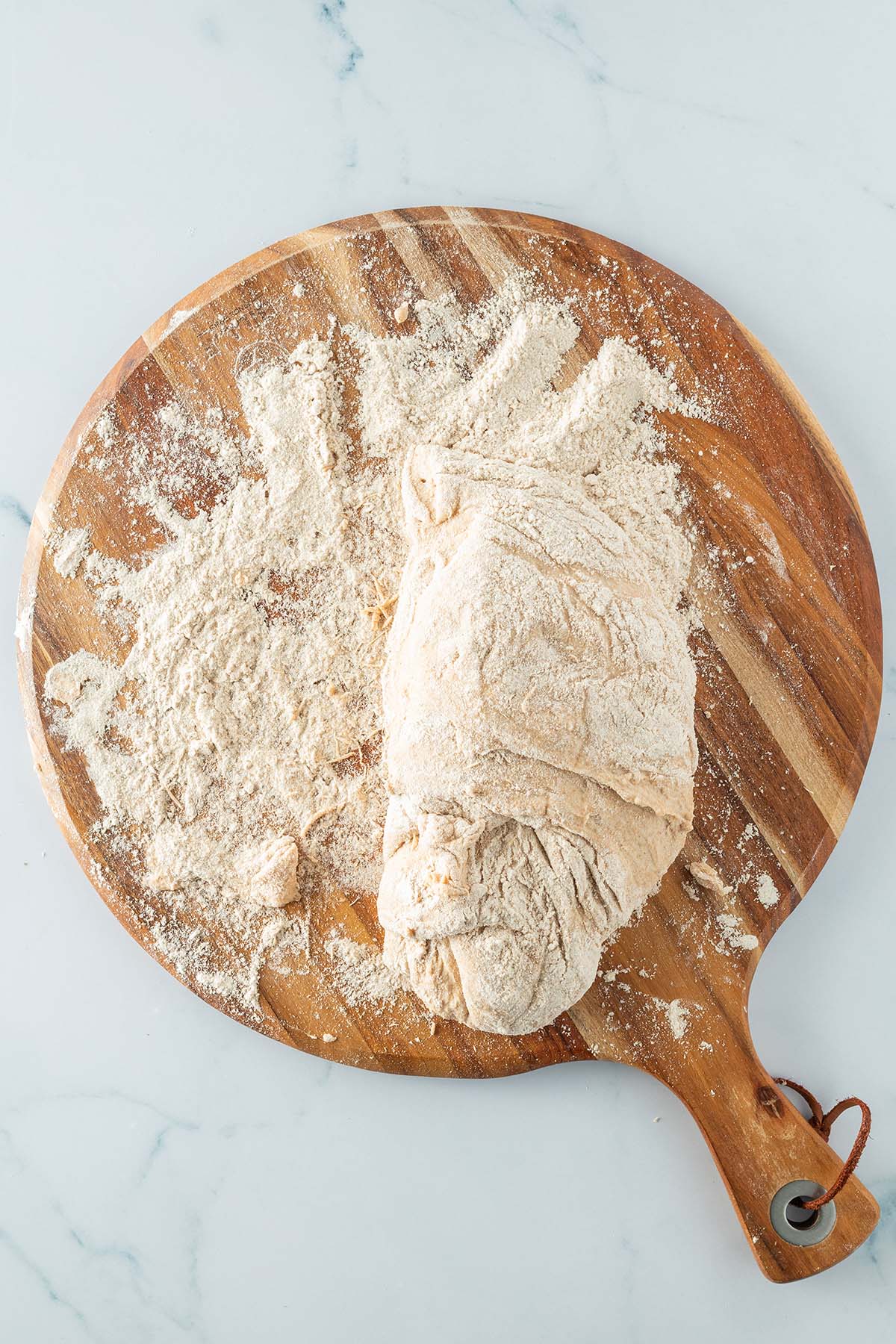 Ein klebriger Teig liegt auf einem stark bemehlten Holzbrett.