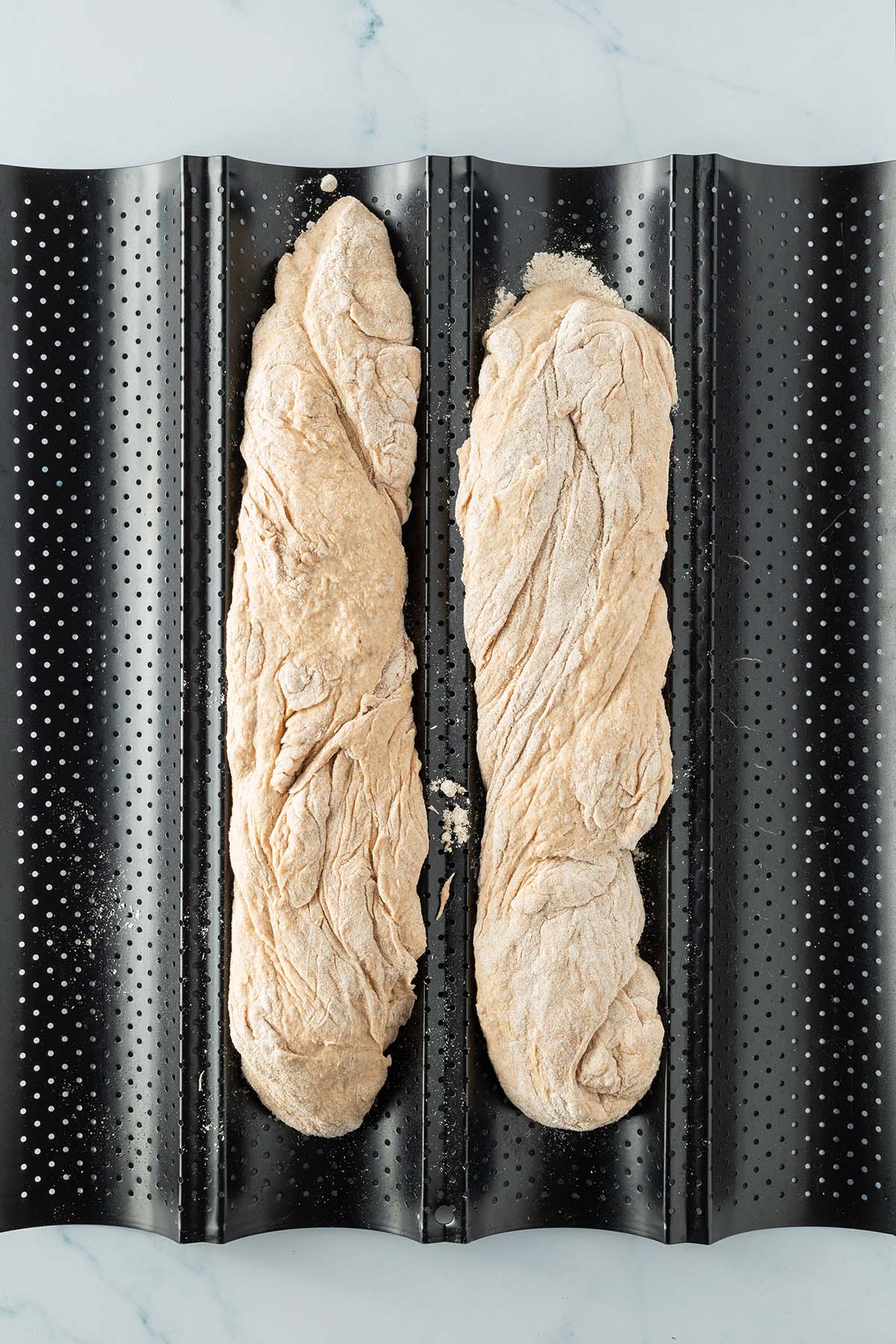 Vogelperspektive auf ein Baguetteblech mit zwei Baguette-Broten vor dem Backen.