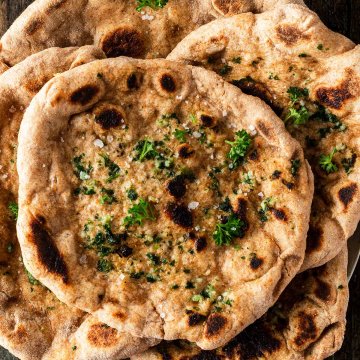 Mehrere Naan Brote mit aufeinander gestapelt auf einem dunklen Holzuntergrund.