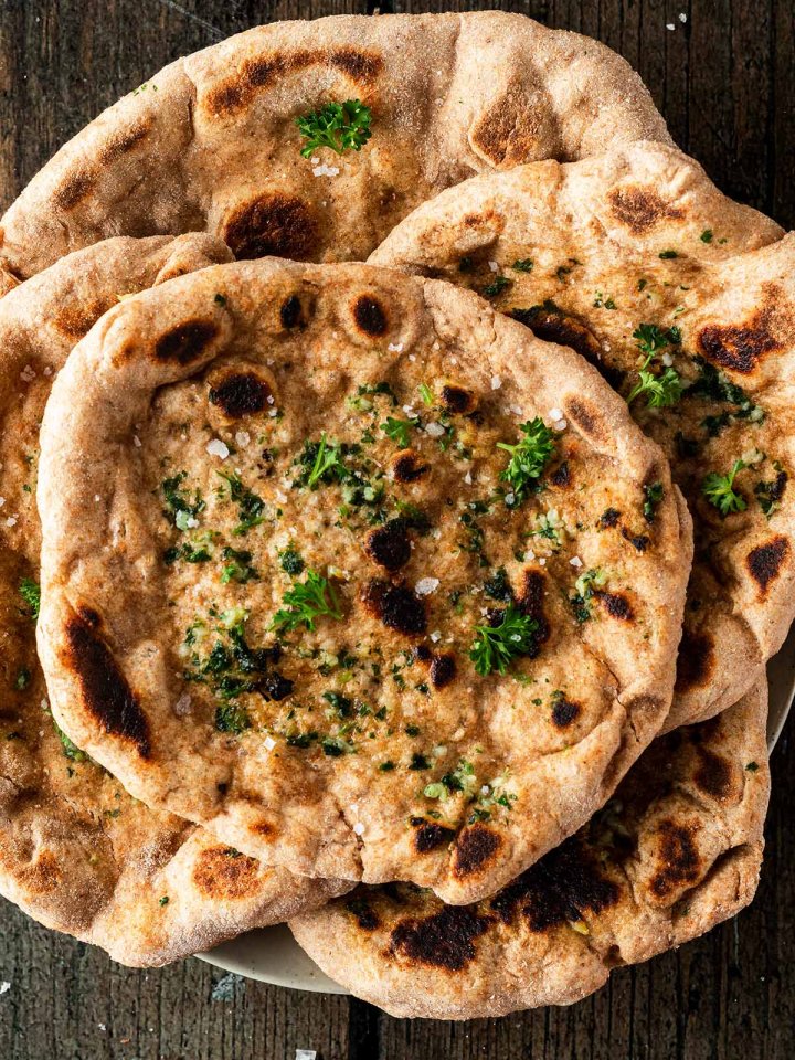 Mehrere Naan Brote mit aufeinander gestapelt auf einem dunklen Holzuntergrund.