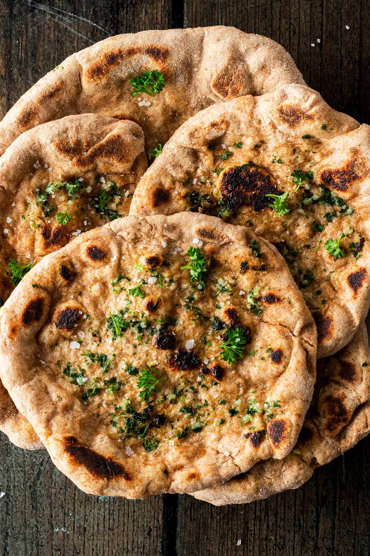 Mehrere Naan Brote mit Knoblauch und Kr&auml;utermarinade auf einem Holzuntergrund.