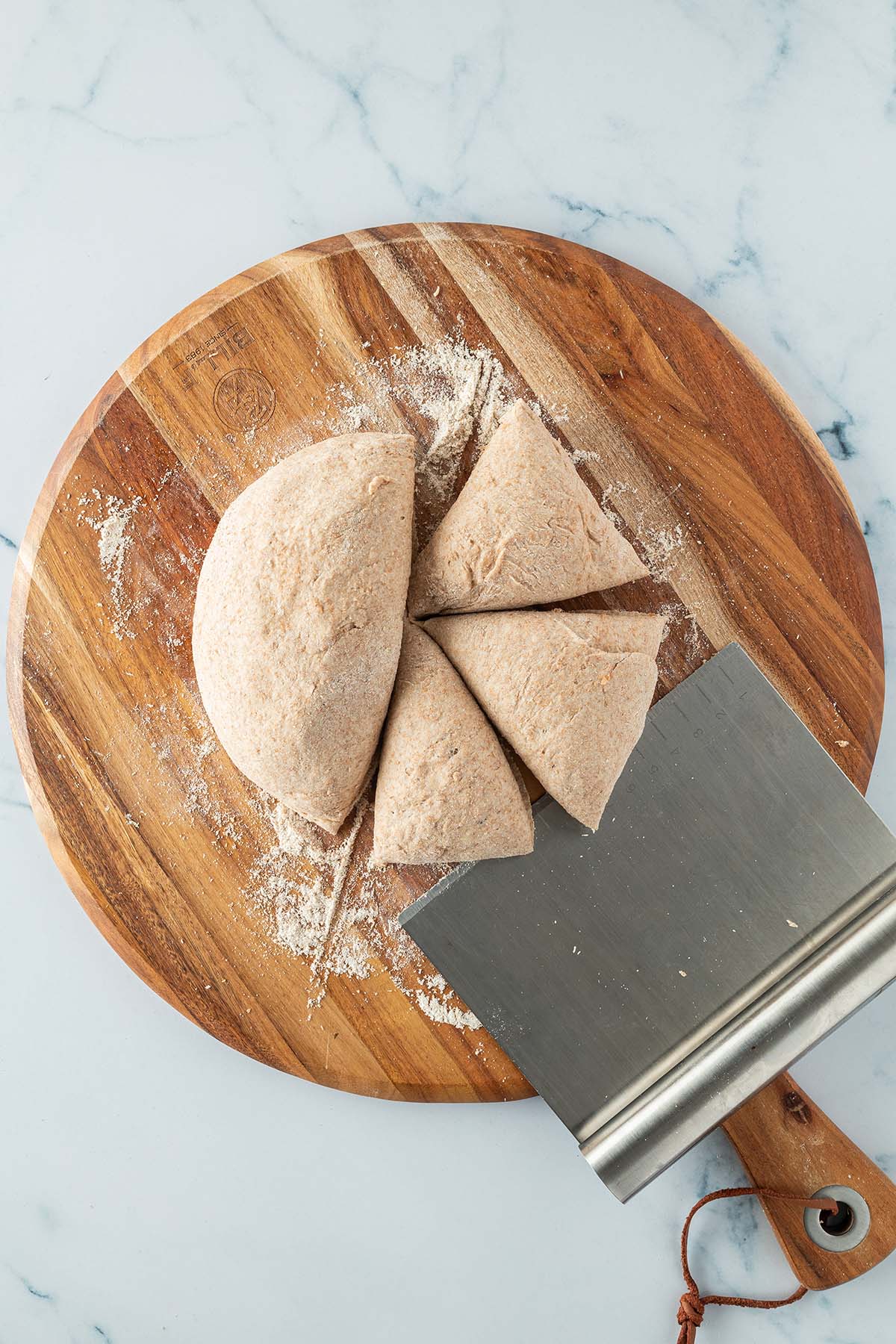 Ein zu einer Kugel geformter und in vier Teile geteilter Hefeteig auf einem Holzbrett mit einer Teigkarte daneben.
