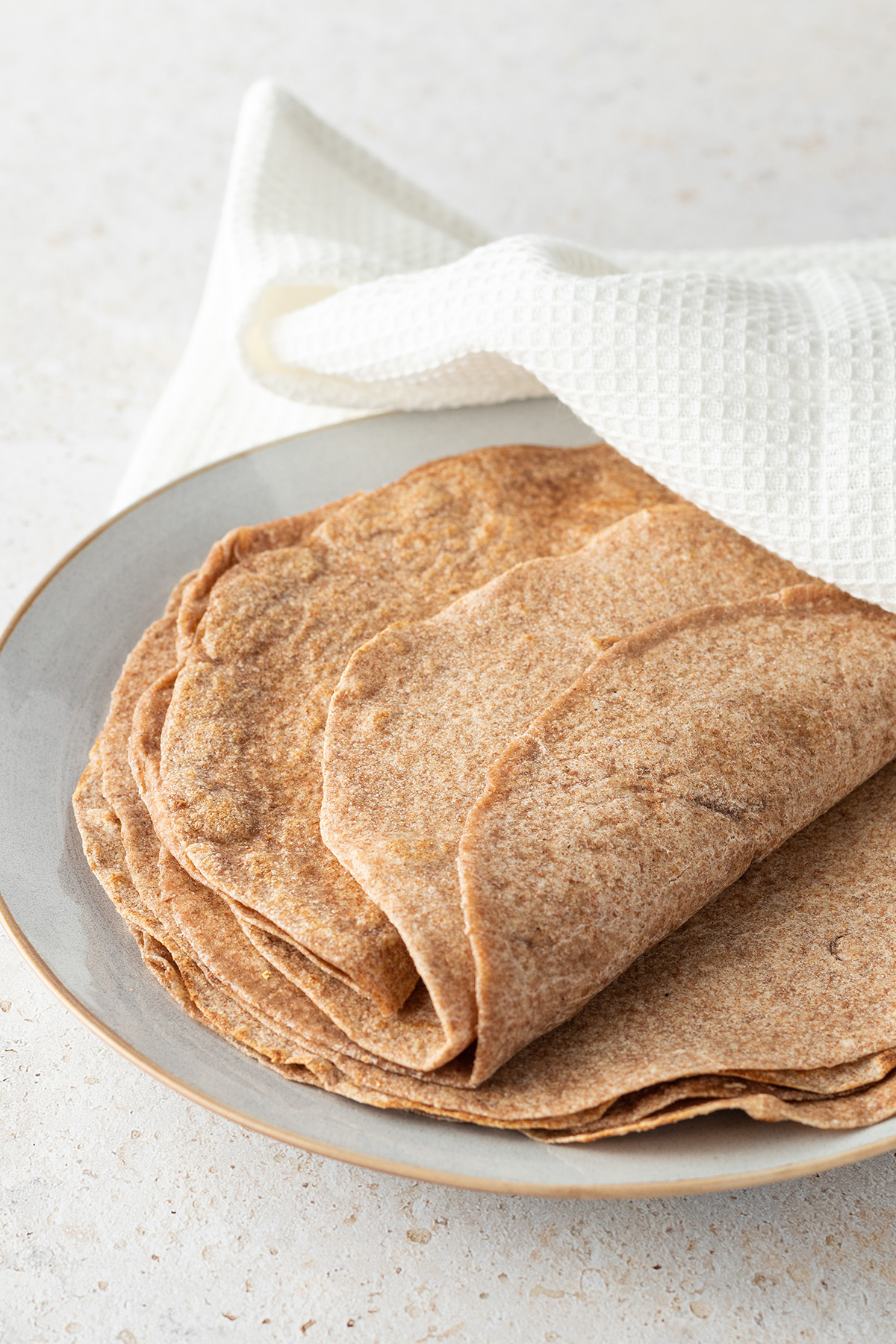 Ein Stapel aus Tortilla Wraps auf einem Teller, halb mit einem wei&szlig;en Geschirrtuch bedeckt.