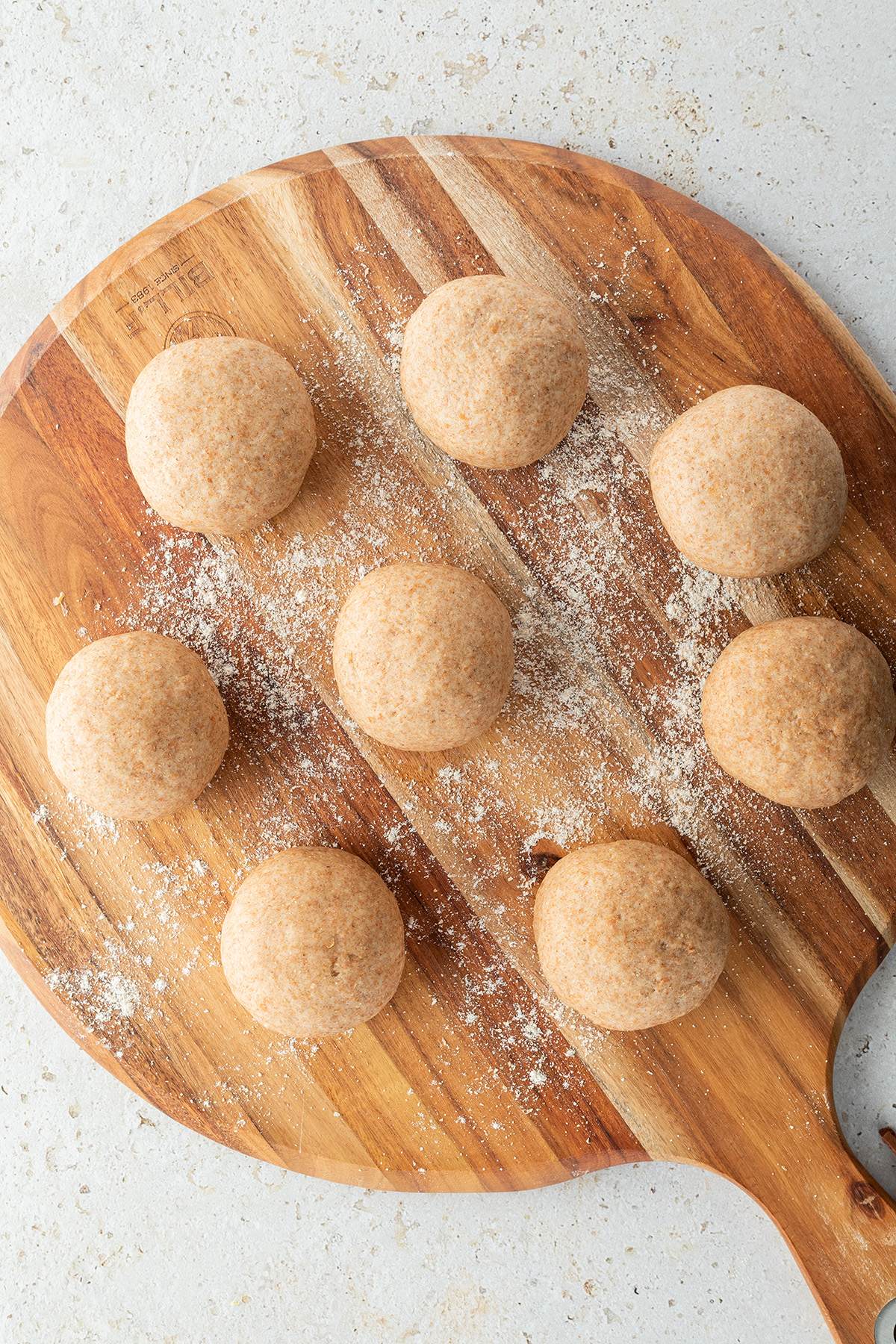 Acht gleich gro&szlig;e Teigb&auml;llchen auf einem Holzbrett,