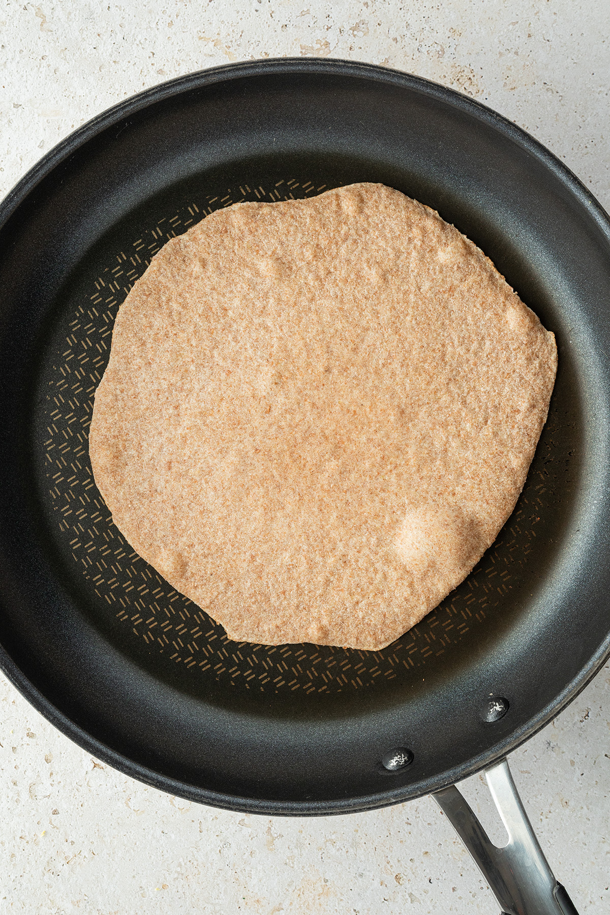 Tortilla Wrap in einer gro&szlig;en Beschichteten Pfanne, auf dessen Oberseite sich kleinere und gr&ouml;&szlig;ere Blasen gebildet haben.