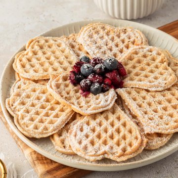 Ein Teller mit d&uuml;nnen, herzf&ouml;rmigen Waffeln, serviert mit frischen und hei&szlig;en Beeren mit Deko.
