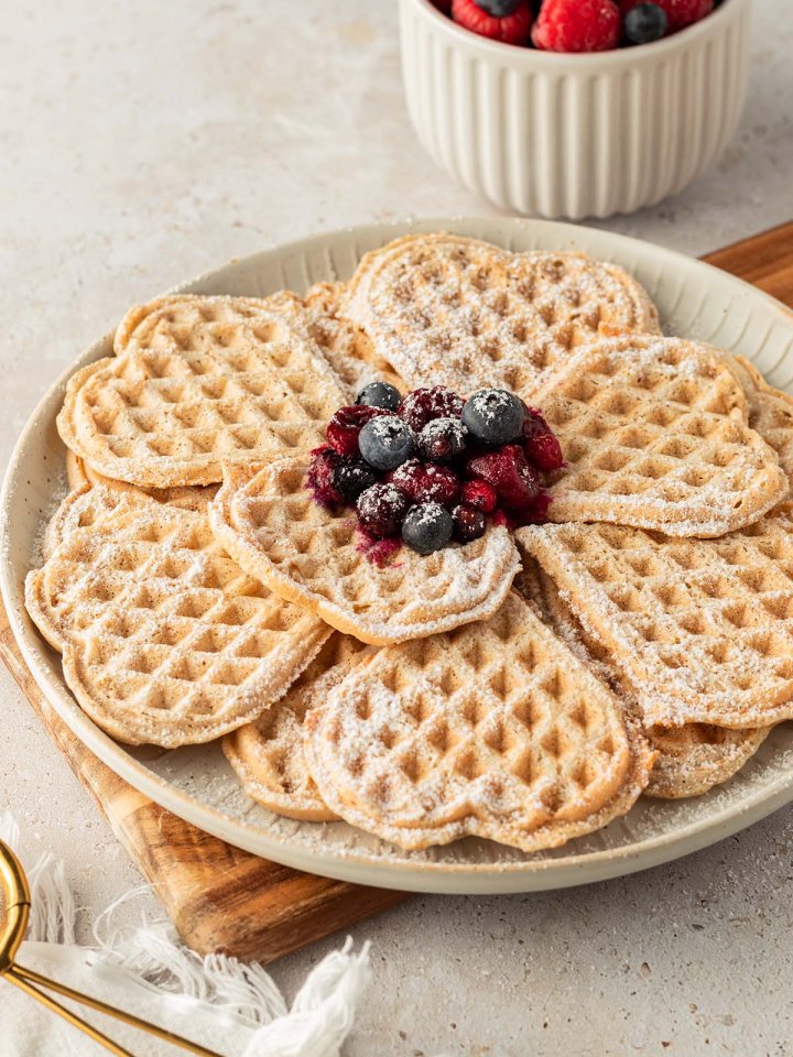 Ein Teller mit d&uuml;nnen, herzf&ouml;rmigen Waffeln, serviert mit frischen und hei&szlig;en Beeren mit Deko.