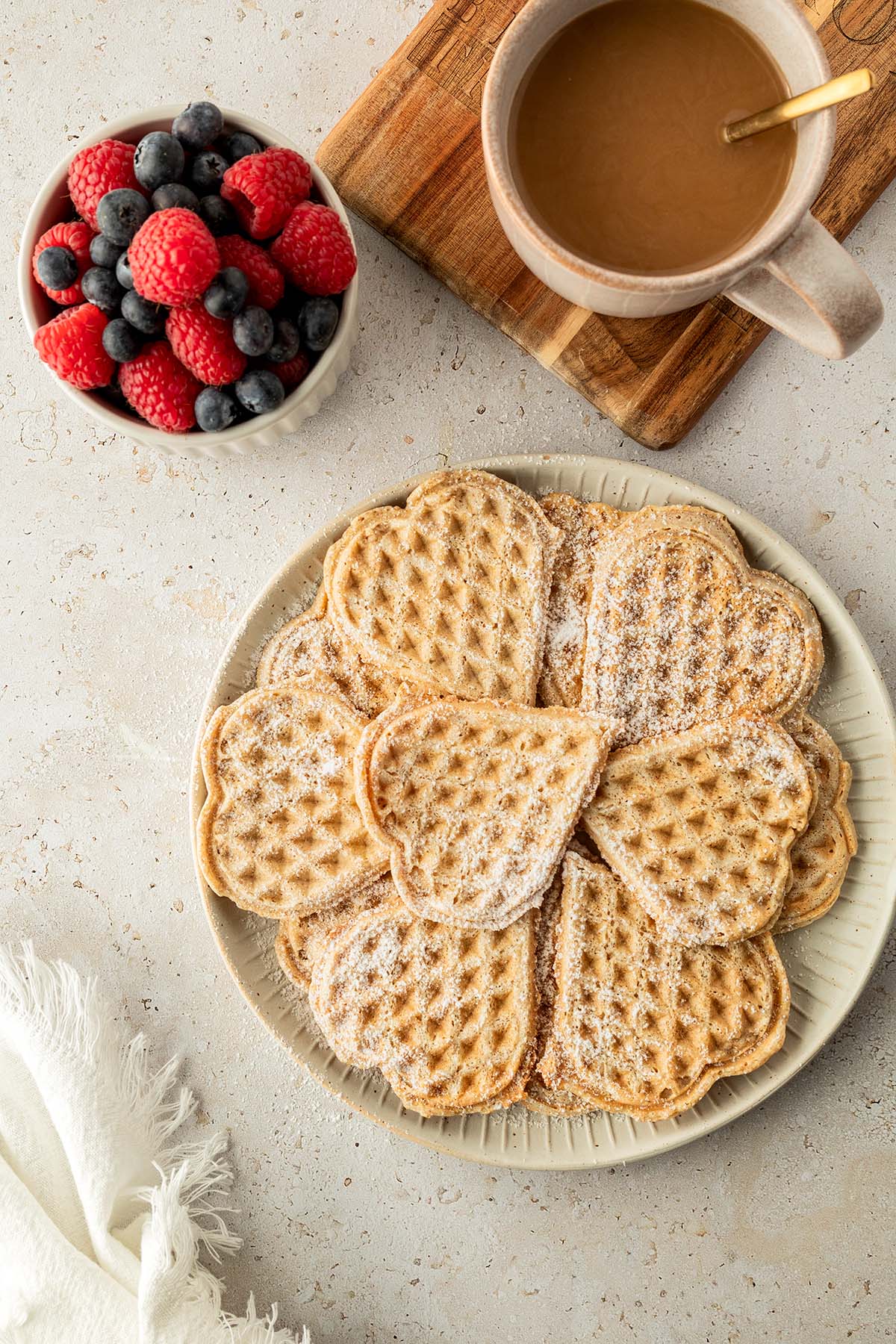Ein Teller mit Waffeln, daneben eine Tasse Kaffee und eine Sch&uuml;ssel mit frischen Beeren.