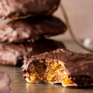 Angebissener weicher Elisenlebkuchen mit Schokoglasur, mehr Lebkuchen im Hintergrund.