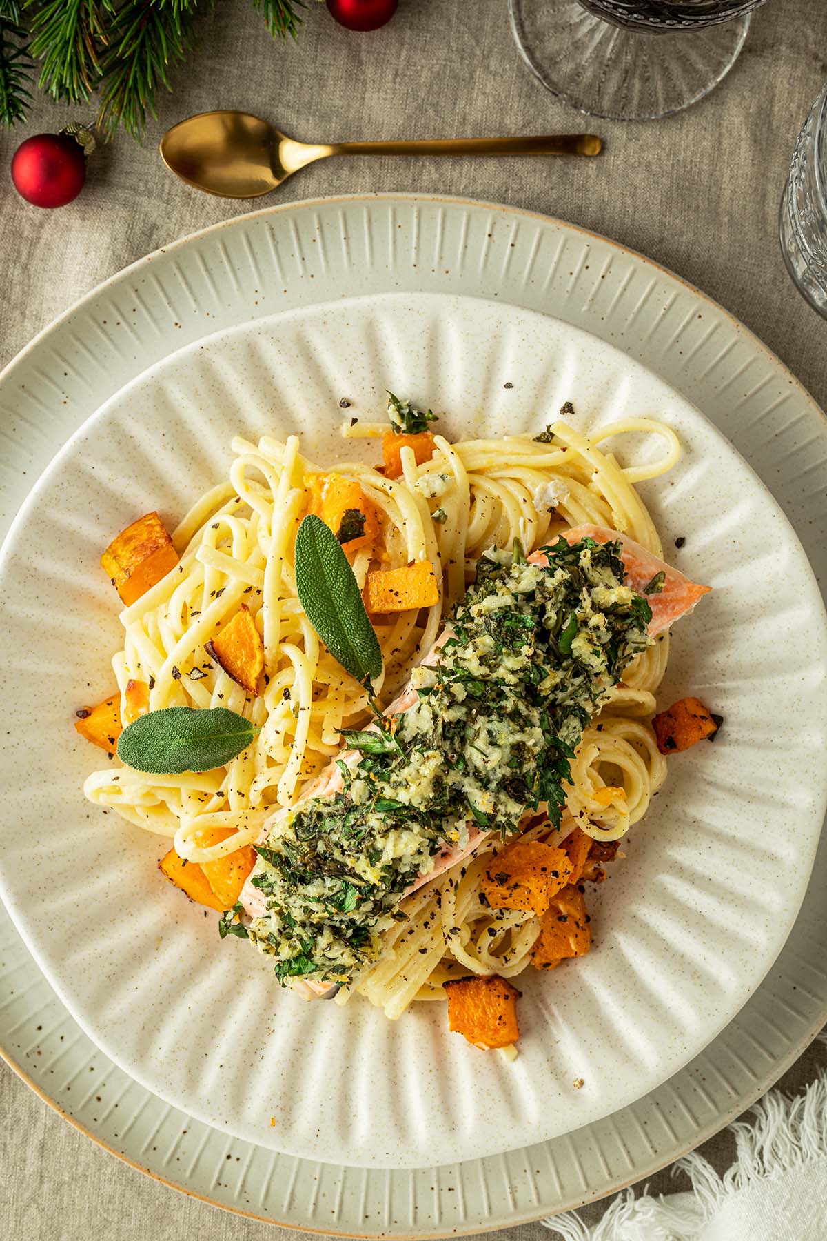 Lachs mit Kr&auml;uterkruste serviert auf einer cremigen Pasta mit K&uuml;rbisw&uuml;rfeln auf ein weihnachtlich gedecktem Tisch.