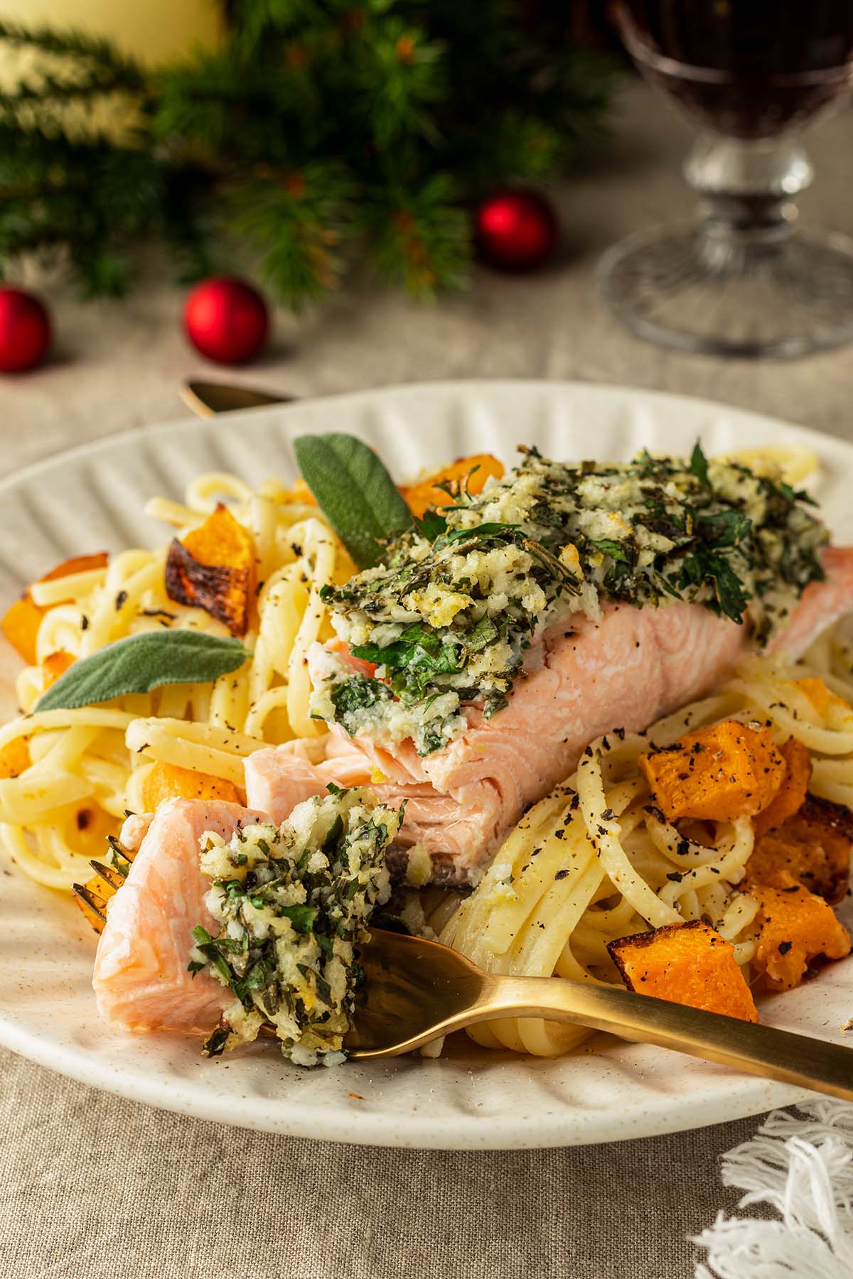 Frontansicht auf ein Teller mit Lachsfilet und Kr&auml;uterkruste auf cremiger Zitronenpasta mit K&uuml;rbis.