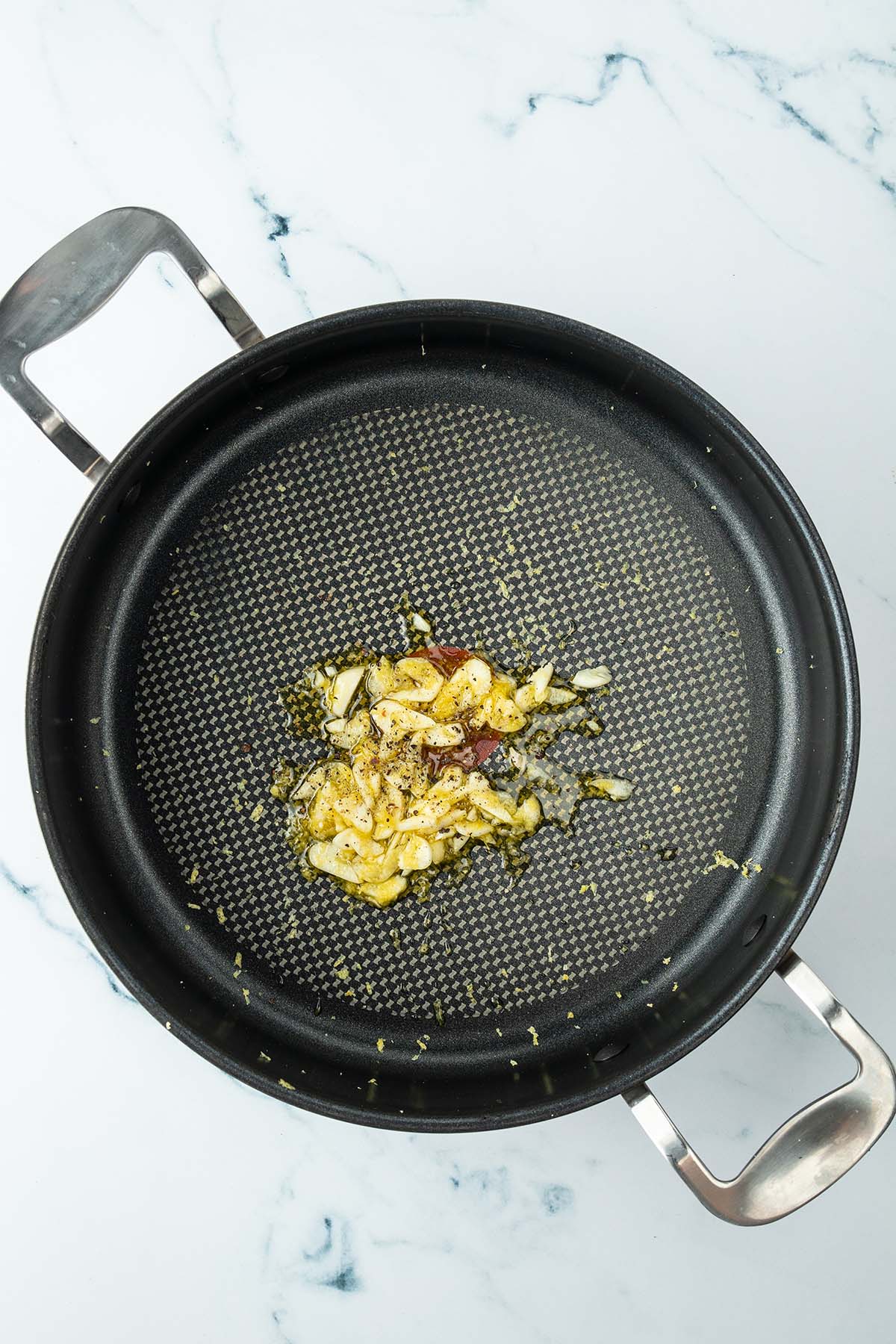 D&uuml;nne Knoblauchscheiben, Zitronenabrieb und Oliven&ouml;l in einer gro&szlig;en Pfanne.