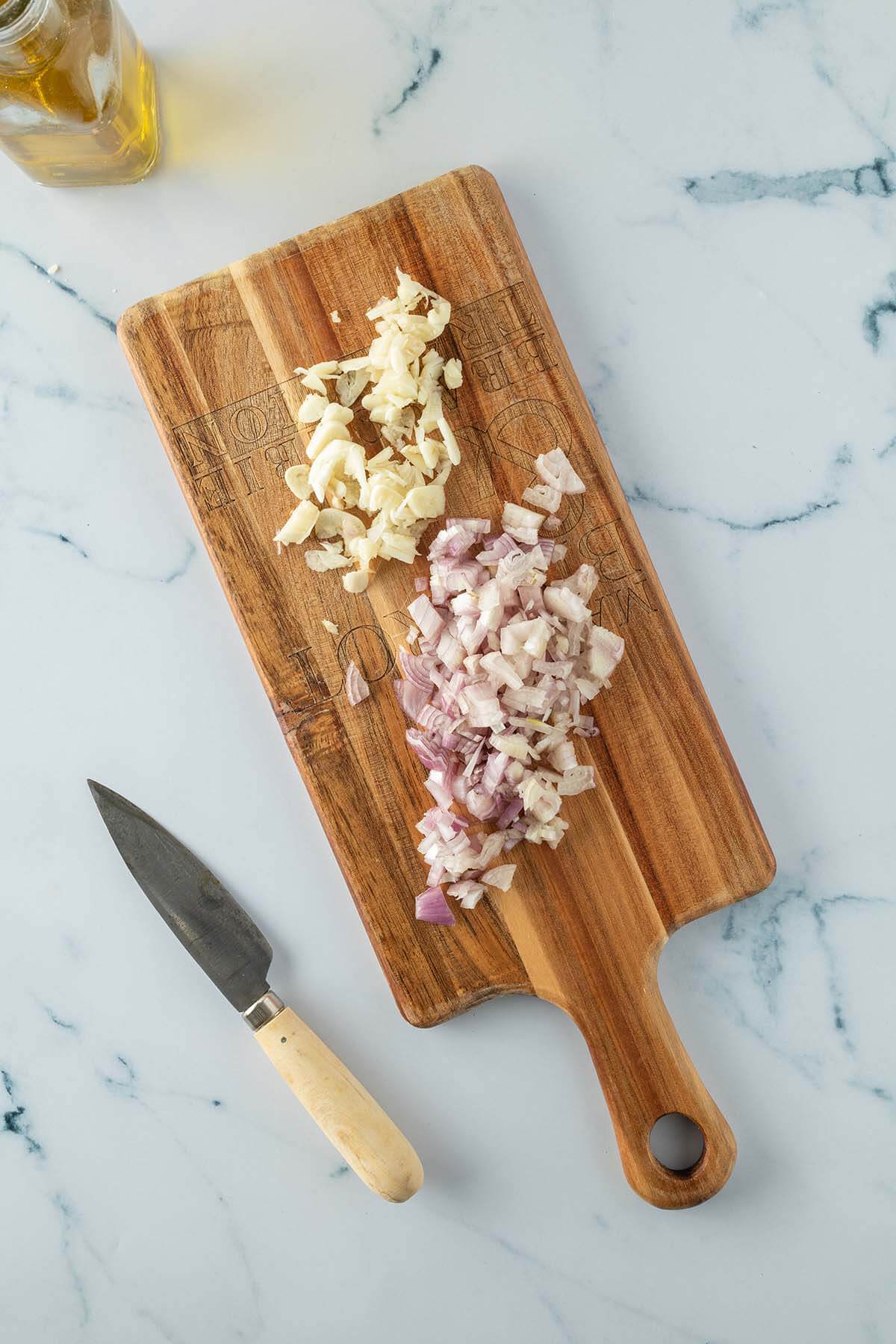 Fein gew&uuml;rfelte Schalotten und Knoblauchzehen auf einem Holzbrett.