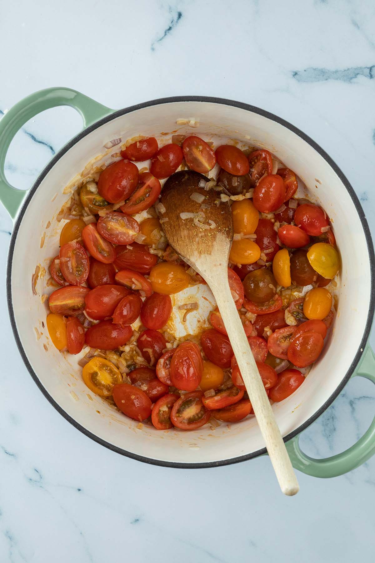 Vogelperspektive auf einen Topf mit halbierten Cherrytomaten und glasigen Schalottenw&uuml;rfeln.