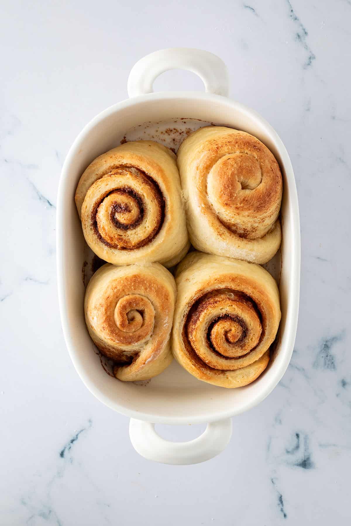 Vier frisch gebackene, goldbraune Zimtschnecken in einer kleinen wei&szlig;en Auflaufform.