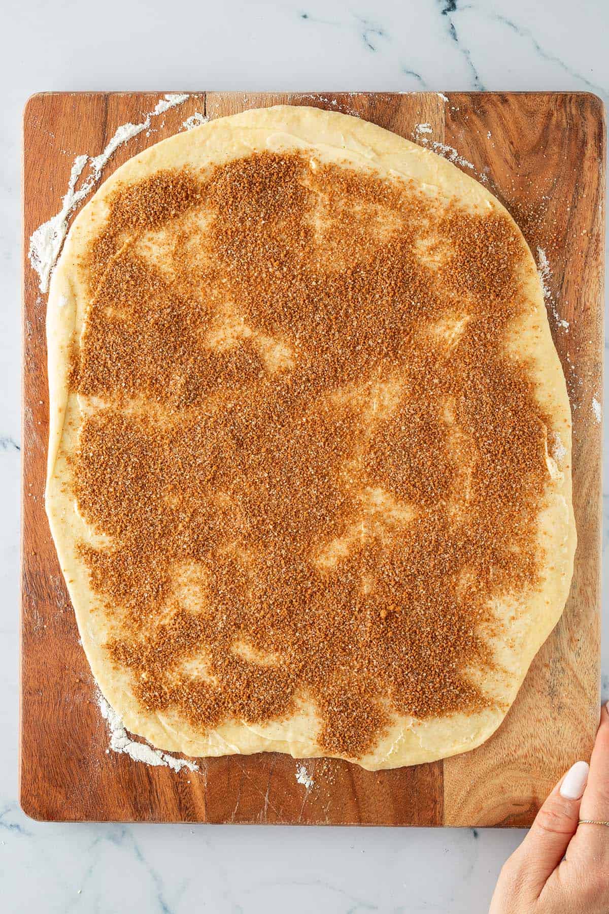 Ausgerollter Hefeteig auf einem Holzbrett, gleichm&auml;&szlig;ig mit Zimt-Zucker-Mischung bestreut.