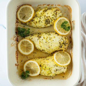 Drei Zitronen-H&auml;hnchenfilets in einer Auflaufform mit Zitronenscheiben und Petersilie.