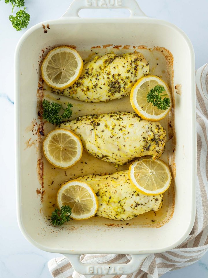 Drei Zitronen-H&auml;hnchenfilets in einer Auflaufform mit Zitronenscheiben und Petersilie.
