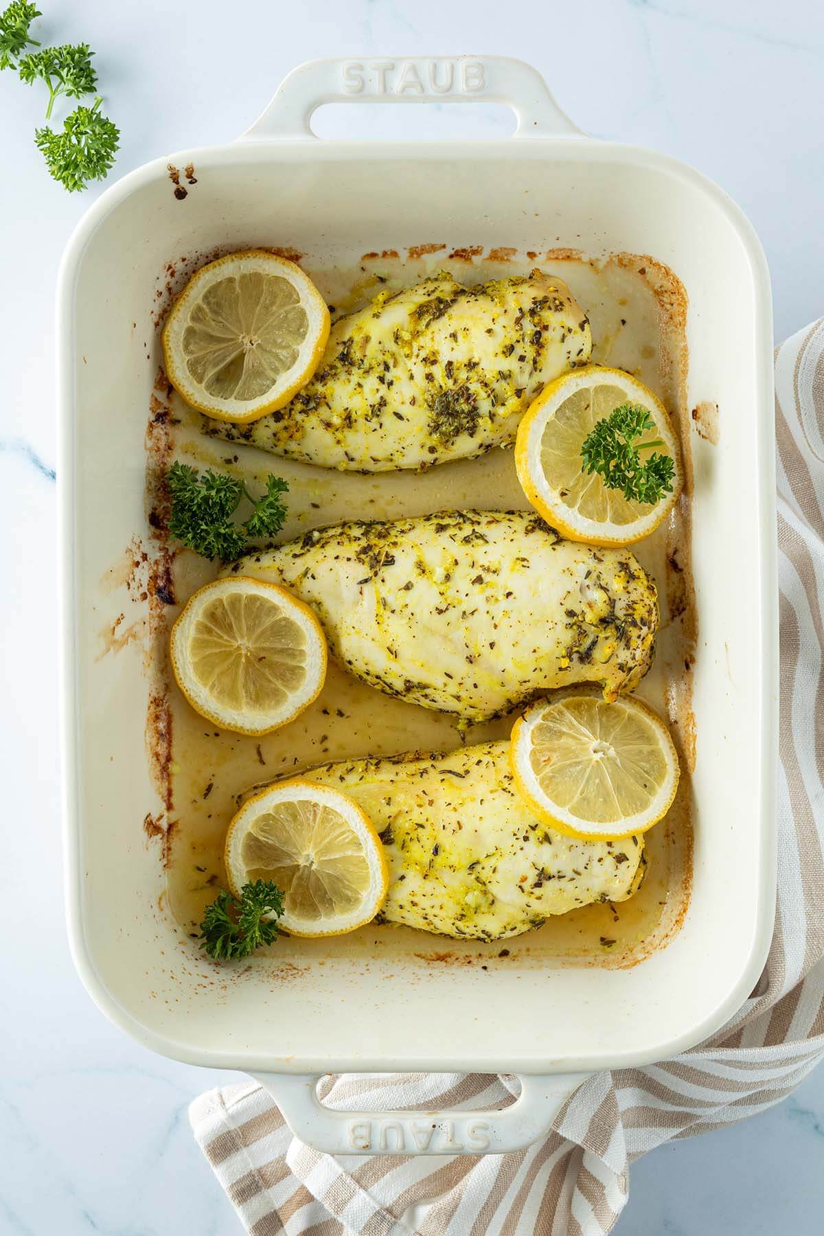 Drei Zitronen-H&auml;hnchenfilets in einer Auflaufform mit Zitronenscheiben und Petersilie.