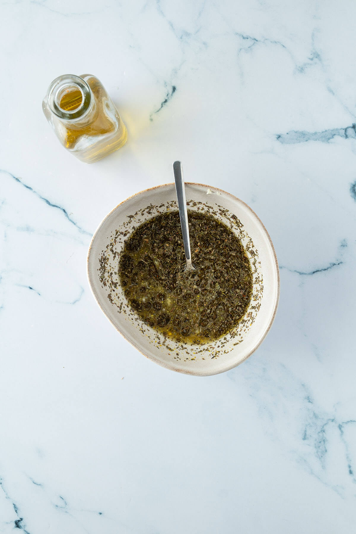 Eine Sch&uuml;ssel mit einer Kr&auml;utermarinade, daneben eine Flasche &Ouml;l.