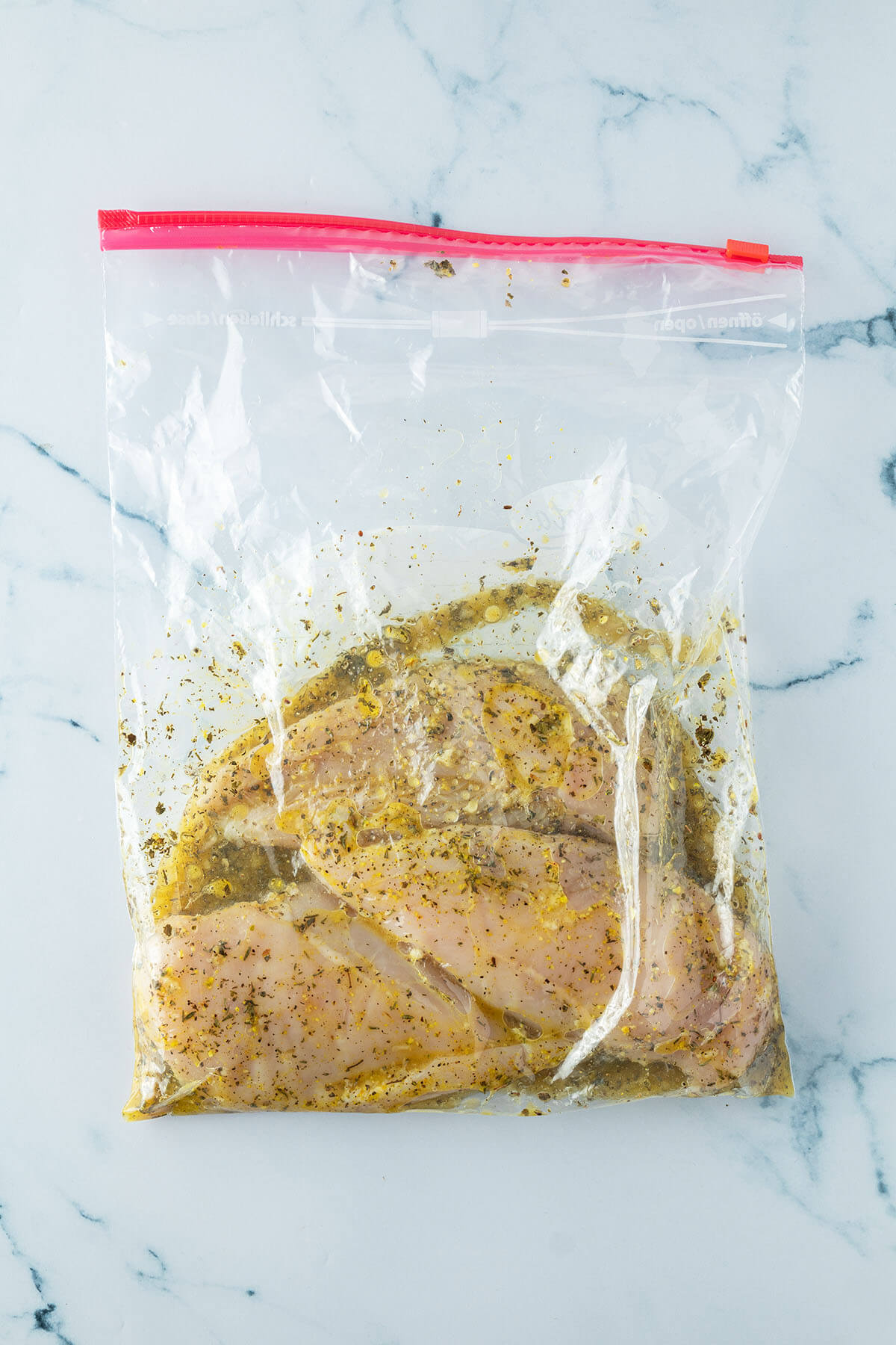Rohe H&auml;hnchenfilets in einem Zip-Beutel mit einer Zitronen-Kr&auml;uter-Marinade.