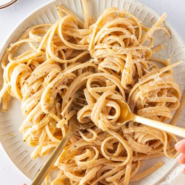 Vogelperspektive auf einen Teller mit Linguine in einer cremigen Sauce, wo zwei H&auml;nde einen Bissen Nudeln auf eine Gabel aufrollen.