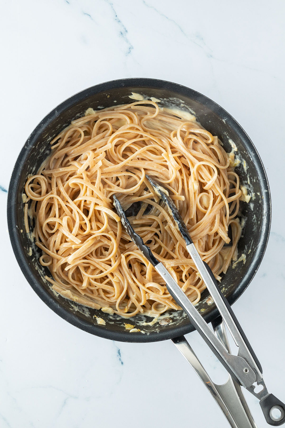 Vogelperspektive auf eine Pfanne, in der Linguine mit einer cremigen Zitronensauce verr&uuml;hrt werden.