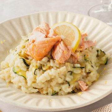 Ein Teller mit cremigen Risotto mit Zitrone, Zucchini uns saftigem Lachsst&uuml;ckchen.